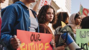 Teenage girl holding a megaphone while marching for climate justice with a group of demonstrators. Multicultural youth activists protesting against global warming and climate change.